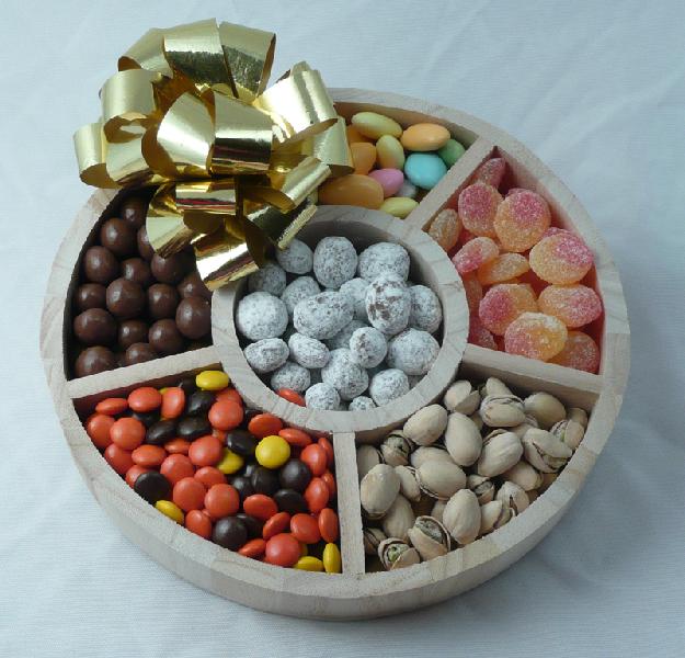 Wooden Tray | Six Confections - This sturdy round wooden tray is filled with six different confections: jordan almonds, sour peaches, pistachios, assorted candies, chocolate covered coffee beans and chocolate covered praline pecans. Shrink wrapped with a large bow.
