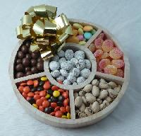 Wooden Tray | Six Confections - This sturdy round wooden tray is filled with six different confections: jordan almonds, sour peaches, pistachios, assorted candies, chocolate covered coffee beans and chocolate covered praline pecans. Shrink wrapped with a large bow.
